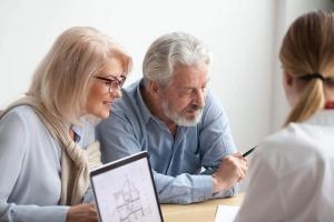Mature couple at a wooden table reviewing legal documents and property deeds for a house sale before probate.